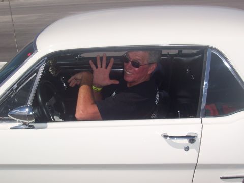 1972 Ford Ranchero - Man waves from the interior of a white 1965 Ford Mustang coupe.