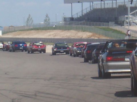 1972 Ford Ranchero - A line of vehicles waits on a racetrack, with grandstands visible in the background.