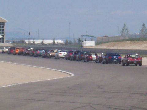 1972 Ford Ranchero - Multiple cars lined up on a paved track with a building and hills in the background.