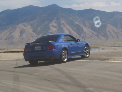 1972 Ford Ranchero - Blue coupe with a spoiler is seen from the rear on a track, with mountains in the background. The license plate is visible.