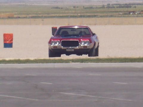 1972 Ford Ranchero - A red 1972 Ford Ranchero is seen from the front, parked on a sandy area with a grassy strip in the foreground.