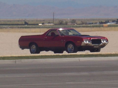 1972 Ford Ranchero - A red 1972 Ford Ranchero is parked on a dirt lot with a highway in the foreground.