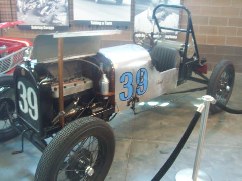 1972 Ford Ranchero - A vintage race car with exposed mechanicals and a roll cage is displayed indoors.