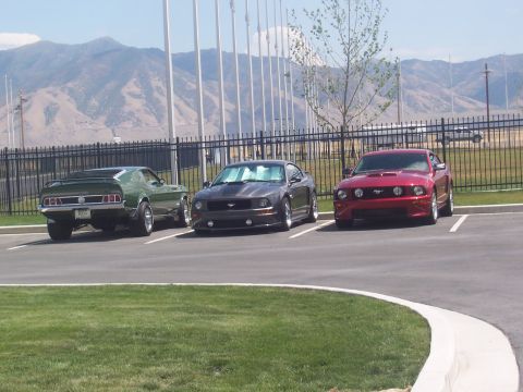 1972 Ford Ranchero - Three Ford Mustangs, one classic and two modern, are parked in a lot with mountains in the background.