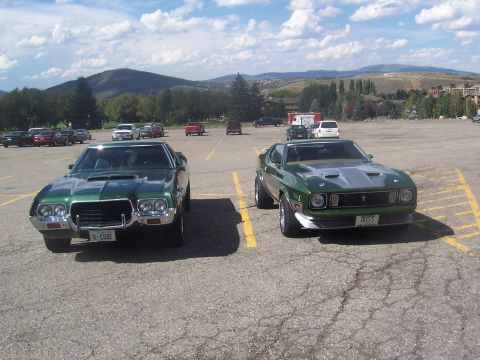 1972 Ford Ranchero - A green 1971 Ford Mustang Mach 1 is parked next to another green muscle car in a parking lot.
