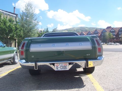 1972 Ford Ranchero - Rear view of a green 1972 Ford Ranchero GT parked in a lot with buildings and mountains in the background.