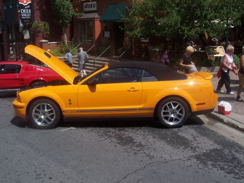 1972 Ford Ranchero - Yellow convertible Mustang GT 500 with hood open, parked on a street next to a red car.
