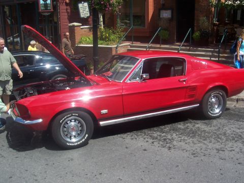 1972 Ford Ranchero - A red 1967 Ford Mustang coupe is parked on a street with its hood open, with other vehicles and buildings in the background.