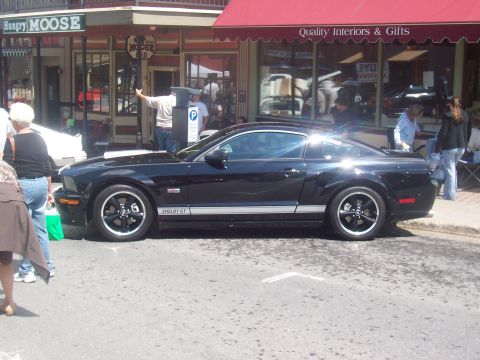 1972 Ford Ranchero - A black Ford Mustang Shelby GT is parked on a street in front of shops.