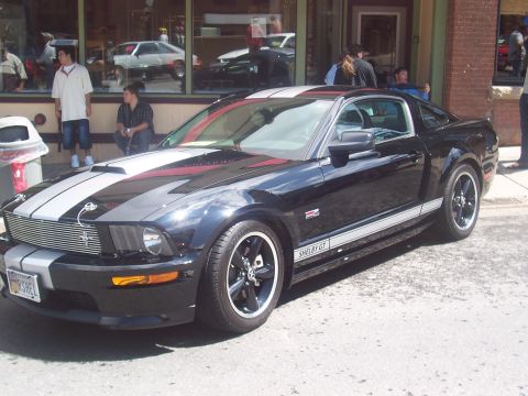 1972 Ford Ranchero - A black Ford Mustang Shelby GT with silver racing stripes is parked on a street in front of a building.