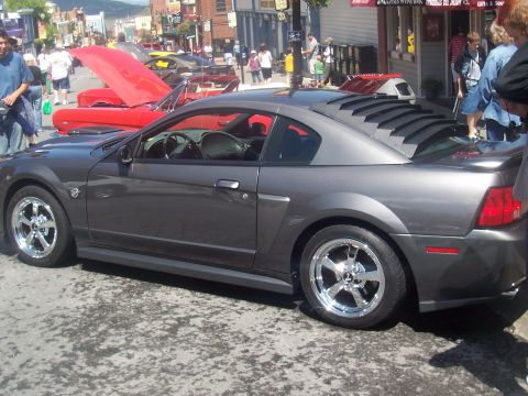 1972 Ford Ranchero - A gray coupe with distinctive rear window louvers is parked on a street during a show.