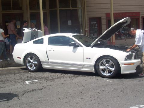 1972 Ford Ranchero - White Ford Mustang Shelby GT parked on street with hood open, people around.
