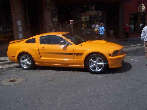 1972 Ford Ranchero - A bright orange Ford Mustang GT/CS is parked on a street in front of shops.