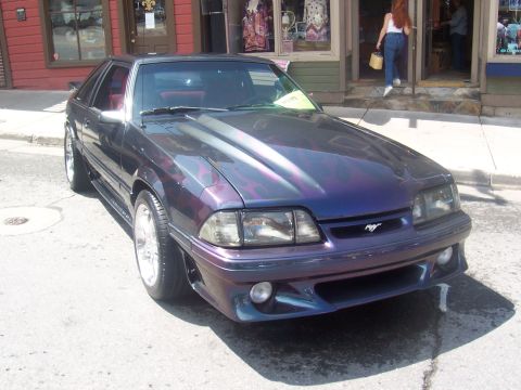 1972 Ford Ranchero - A custom purple Ford Mustang with flame graphics is parked in front of shops.