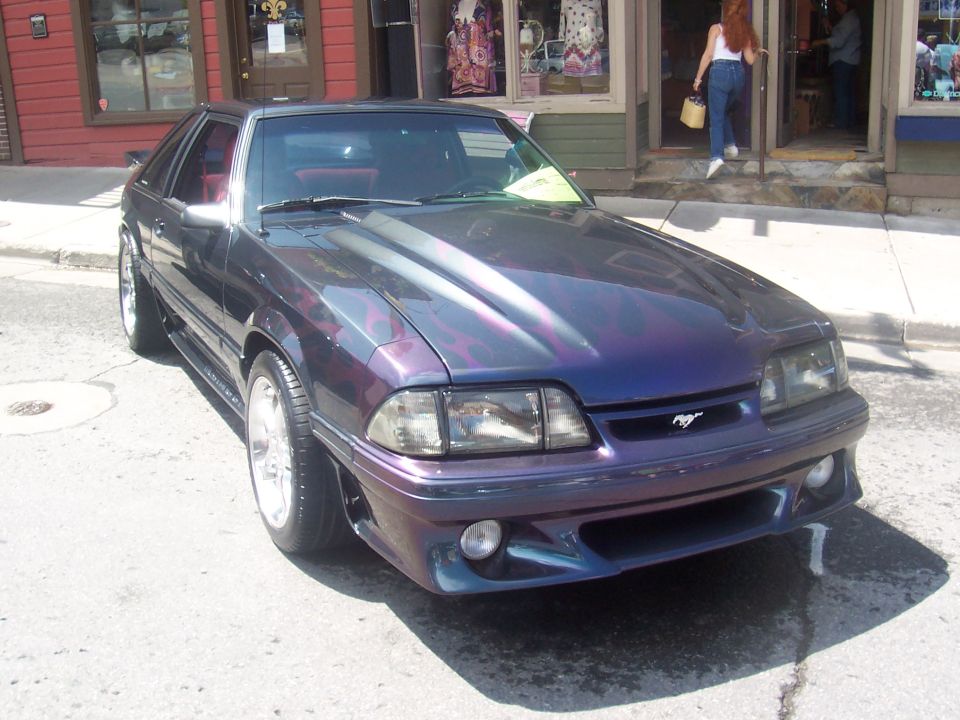 Purple Ford Mustang with flame graphics, custom hood, and body kit, parked on a street