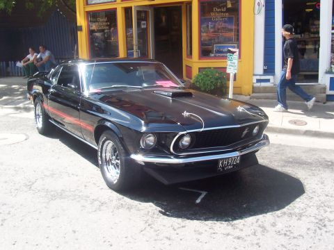 1972 Ford Ranchero - A black 1969 Ford Mustang Mach 1 is parked on a street in front of a gallery.