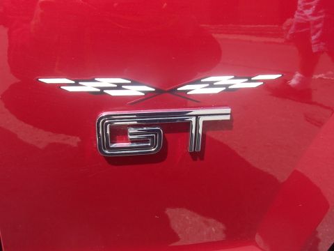 1972 Ford Ranchero - Close-up of a red vehicle's fender displaying a chrome GT emblem and crossed white flag graphics.