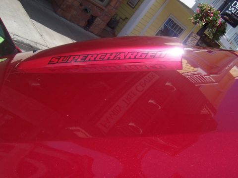 1972 Ford Ranchero - A red vehicle hood features a "SUPERCHARGED" decal, reflecting buildings and signage.