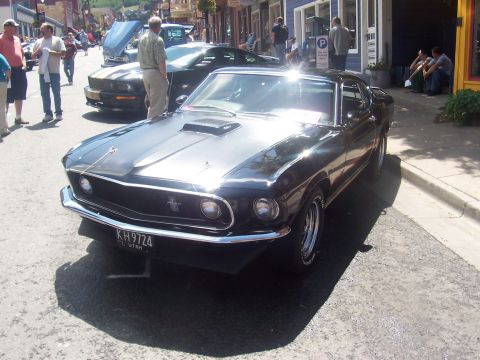 1972 Ford Ranchero - Black 1969 Ford Mustang with hood scoop and chrome bumper, parked on a street with other cars.
