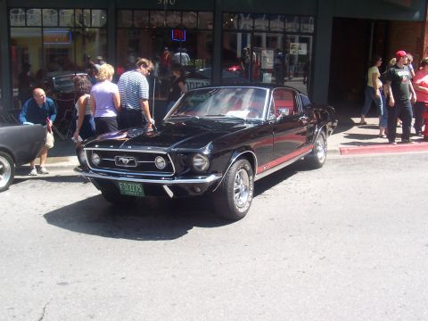 1972 Ford Ranchero - A black 1967 Ford Mustang is parked on a street in front of a building with people around.