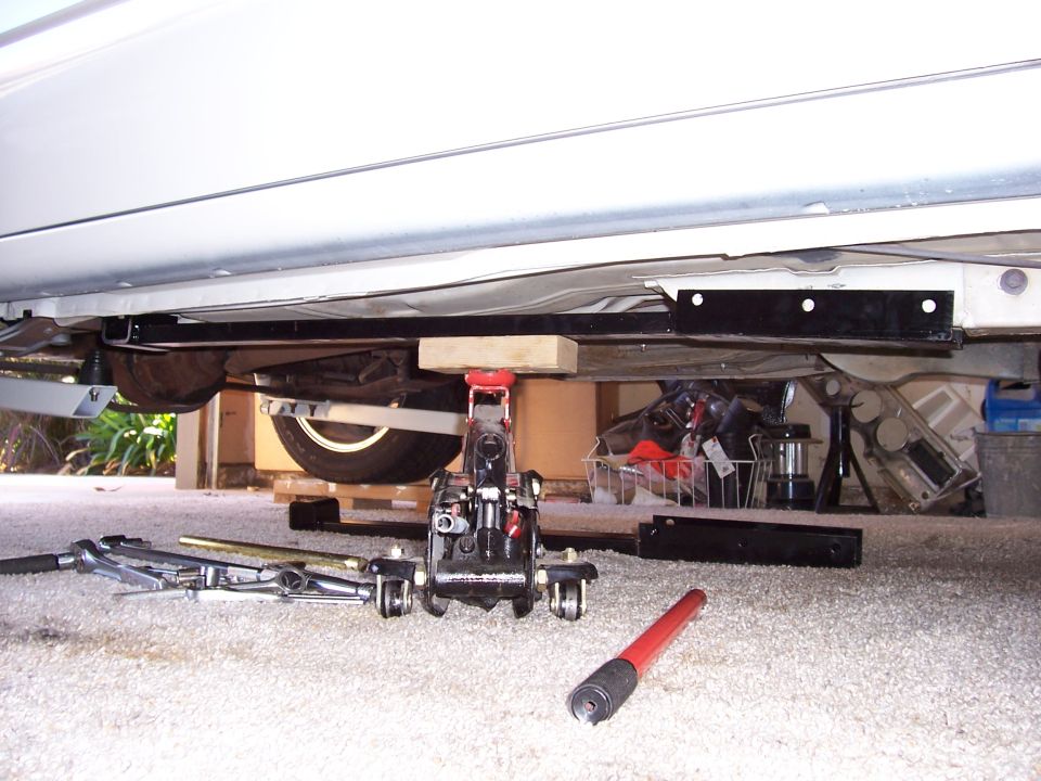 White car undercarriage supported by a jack, with tools on the floor