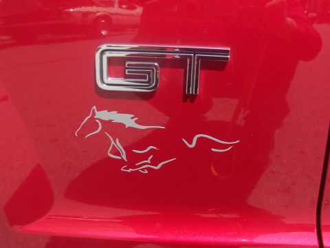 1972 Ford Ranchero - Close-up of a red vehicle's fender, displaying a chrome GT badge and a white running horse emblem.