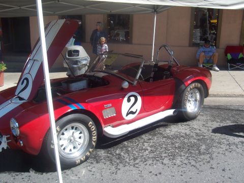 1972 Ford Ranchero - A red convertible sports car with racing stripes is parked under a tent, with people in the background.