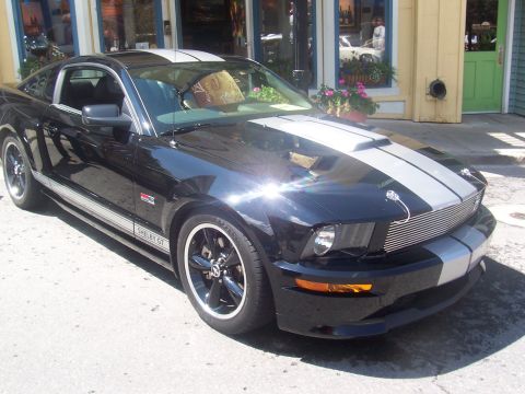 1972 Ford Ranchero - A black Ford Mustang Shelby GT with silver racing stripes is parked in front of a building.