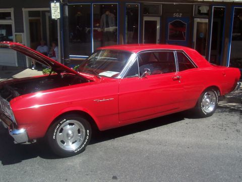 1972 Ford Ranchero - A bright red 1966 Ford Falcon coupe is displayed with its hood up on a street in front of shops.