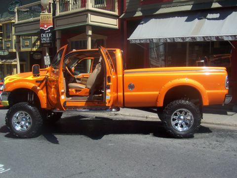 1972 Ford Ranchero - A bright orange pickup truck is parked on a street with its doors open, showing off its interior.
