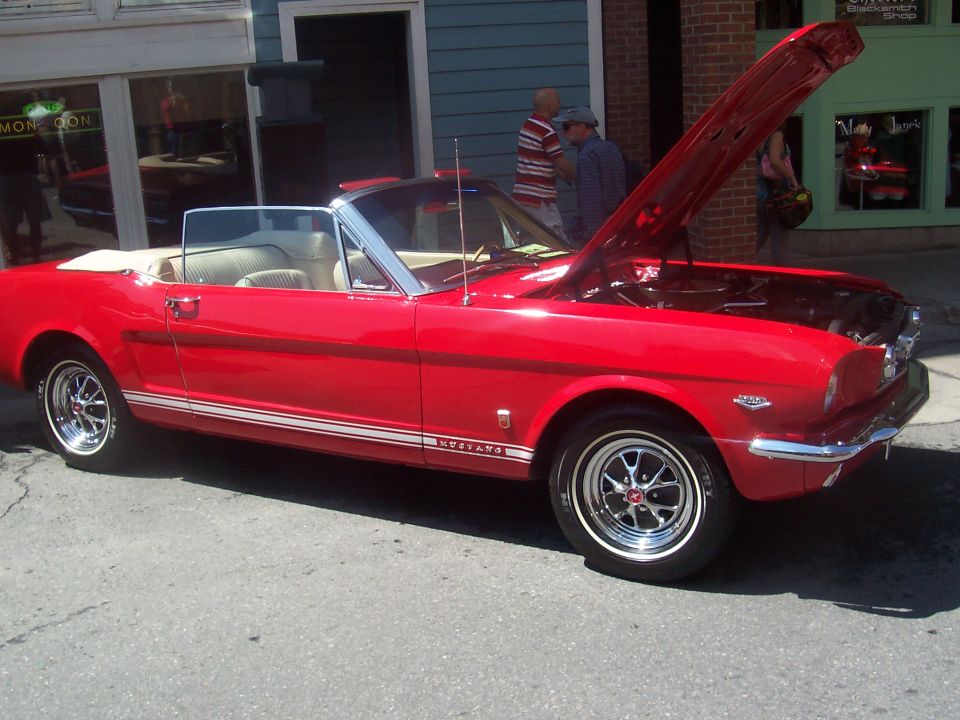 Red convertible classic car with hood open, side view. Has a white stripe along the bottom and 'MUSTANG' text