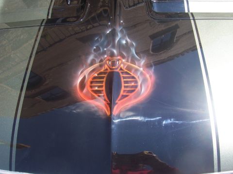 1972 Ford Ranchero - A custom cobra emblem with flames is airbrushed onto the hood of a car with racing stripes.
