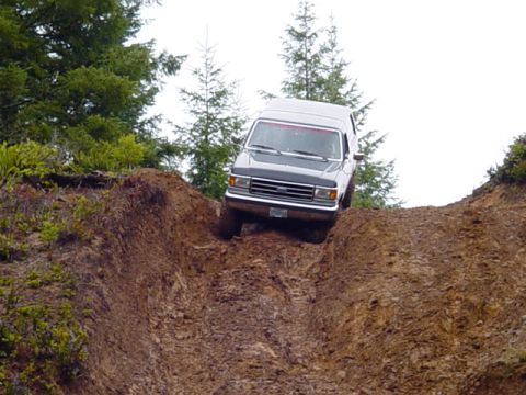 1989 Ford Bronco - A dark gray SUV navigates a steep, muddy incline, its front grille suggesting a 1987 model year.