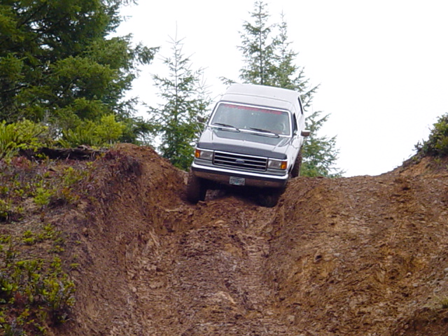 White and gray Ford Bronco at the top of a steep muddy dirt bank, front view
