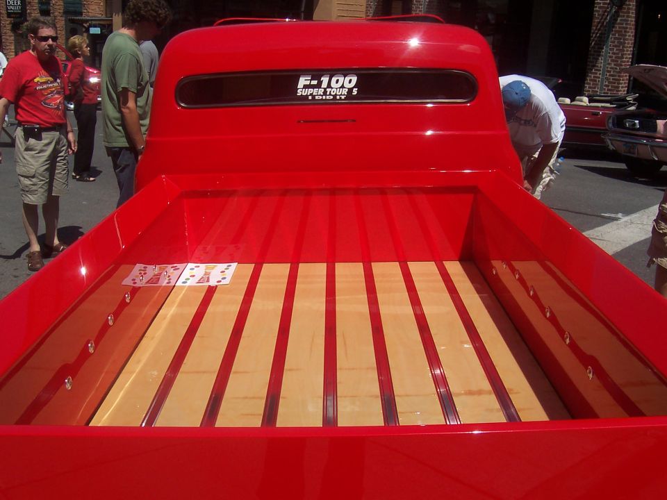 Red pickup truck bed with wood floor. F-100 Super Tour 5 sticker on back window