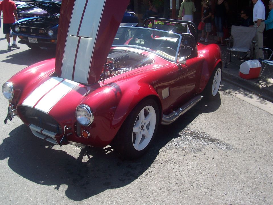 red sports car, hood open showing engine, white racing stripes, white wheels, parked on street