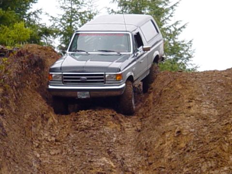 1989 Ford Bronco - This Ford Bronco is navigating a steep, muddy incline on an off-road trail.