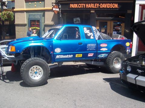 1972 Ford Ranchero - A modified blue pickup truck with racing decals is parked outside a Harley-Davidson dealership.