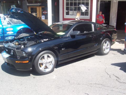 1972 Ford Ranchero - A black Ford Mustang GT is displayed with its hood open, parked next to a blue truck.