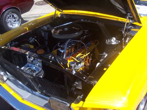1972 Ford Ranchero - The engine bay of a yellow vehicle is open, revealing a V8 engine with chrome detailing and yellow spark plug wires.