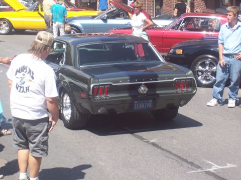 1972 Ford Ranchero - A dark green Ford Mustang is parked on a street with other cars and people around.