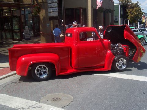 1972 Ford Ranchero - Customized red 1956 Ford F-100 pickup truck with its hood open, displayed on a street.
