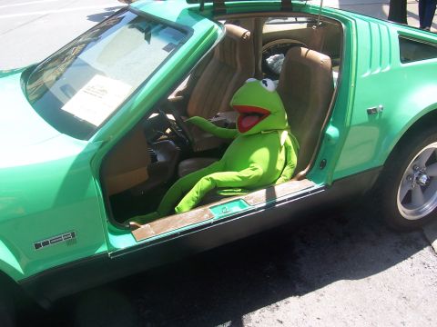 1972 Ford Ranchero - A Kermit the Frog plush toy is positioned in the driver's seat of a green car, appearing to steer.