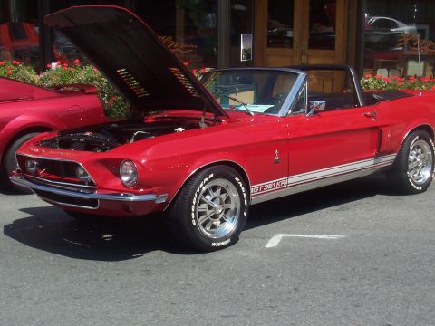 1972 Ford Ranchero - A red convertible with its hood open, parked on a street next to another red vehicle.