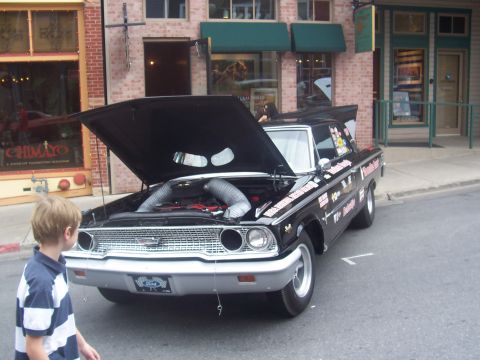 1972 Ford Ranchero - A young boy looks at a modified black Ford sedan with its hood open, parked on a street.