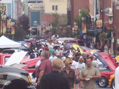 1972 Ford Ranchero - A street is filled with people and cars, many with hoods open, suggesting a car show event.