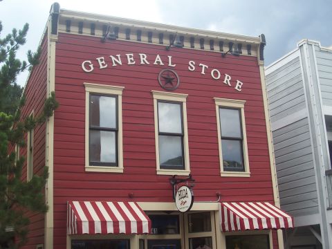 1972 Ford Ranchero - A classic red general store building with white trim and striped awnings stands under a cloudy sky.