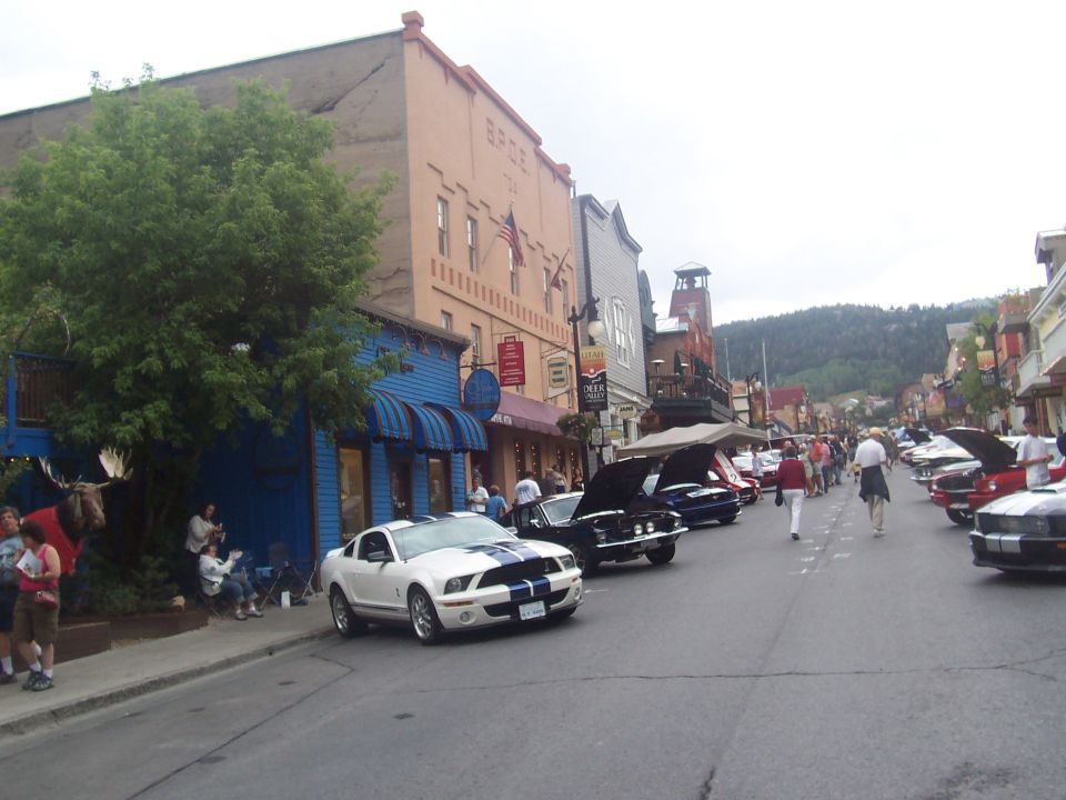 White Ford Mustang with blue stripes parked on street, other cars and buildings in background