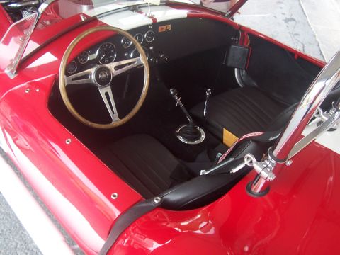 1972 Ford Ranchero - The interior of a classic red sports car features a wooden steering wheel and a manual transmission shifter.