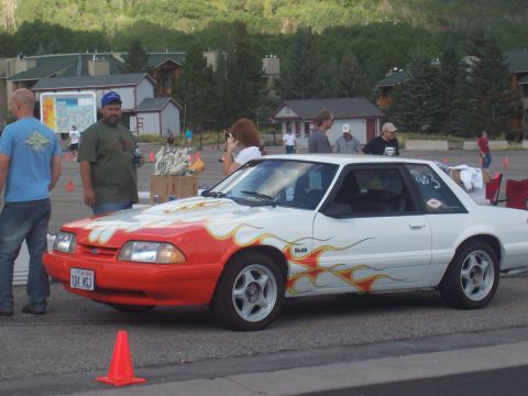 1972 Ford Ranchero - A white coupe with flame decals and a red front bumper is parked on asphalt with people in the background.